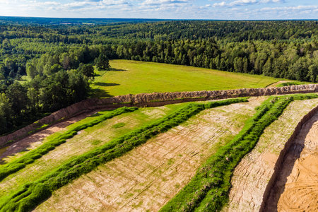 Stripping topsoil at a new sand quarry site, revealing earthworks for mining expansion. Lush summer forest frames the active construction ground from aboveの写真素材