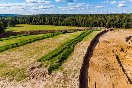 Aerial shot reveals ongoing sand quarry expansion. Overburden is actively stripped from new sections, with heavy machinery bustling on the sunny siteの写真素材