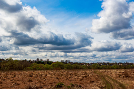 Vast April sky with impressive, brooding clouds hovers above a dry, textured field and a serene,...