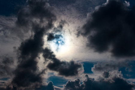Brilliant sun bursts through a thick veil of ominous, dark clouds, casting an ethereal glow on a...