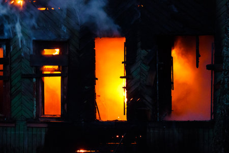 Fiery inferno guts an old derelict wooden house. Bright orange flames and smoke billow from its dark...