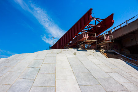 Massive red steel bridge structure dominates the frame, set against a vibrant blue sky. Concrete...