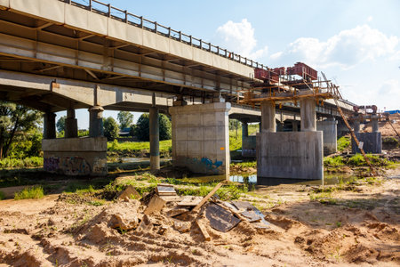Massive concrete and steel bridge structure under extensive reconstruction or major repair during a bright summer day. Essential infrastructure development and maintenance in progressの写真素材