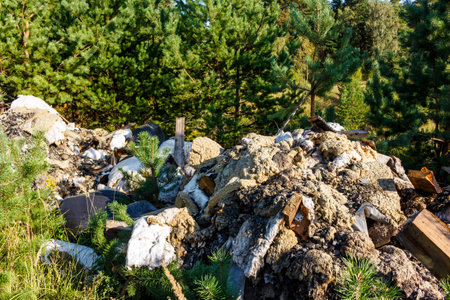Illegal waste dump polluting a vibrant forest. Construction debris and household trash piled high, starkly contrasting with natural greenery on a sunny dayの写真素材