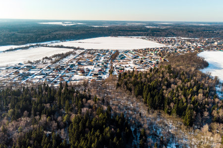 Drone's eye view of a quaint village, homes dotting snowy plains adjacent to evergreen and dormant woodsの写真素材