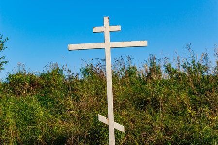Prominent white Orthodox cross rising from vibrant green foliage against a bright blue sky, a symbol of devotion in nature's embrace. Russiaの写真素材