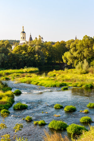 Picturesque view of Borovsk monastery peeking above lush trees, overlooking a serene river with green islets under a clear summer sky. Borovsk, Russiaの写真素材