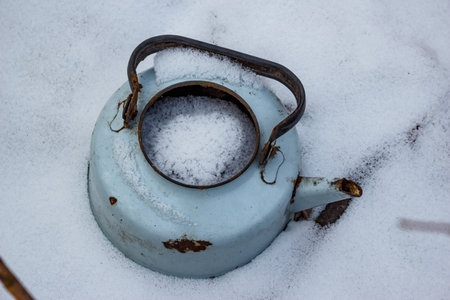 An old abandoned teapot filled with snow in winterの写真素材