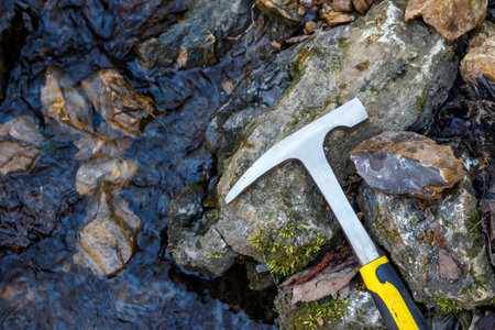 Geological hammer and a striking mineral sample resting on rocks next to a flowing streamの写真素材