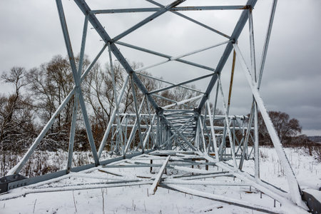 A power line pylon's metallic frame lays covered in fresh snow across a wintry field, awaiting erection. Bare trees dot the cloudy horizonの写真素材