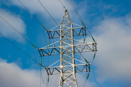 Striking power line pylon structure dominates the frame against a vibrant blue sky with scattered...