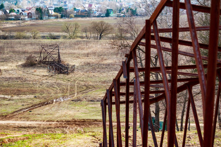 Rusted metal framework of a disassembled power line tower lies on a muddy spring hillside...