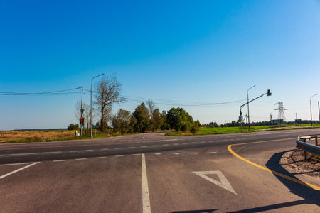 Rural road junction under vast bright blue sky, featuring traffic signals and power lines amidst dry...