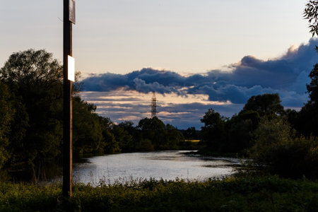 Dramatic summer twilight over a winding river reflecting moody, dark storm clouds with a lone...