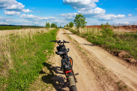 Electric fat bike parked on a sunny dirt road flanked by lush green and dry grass under a bright blue, cloud-strewn sky: Russia - May 20, 2025のeditorial素材