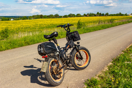 Rugged fat tire electric bike parked on rural asphalt road beside vibrant yellow field under sunny spring sky: Russia - May 20, 2025のeditorial素材