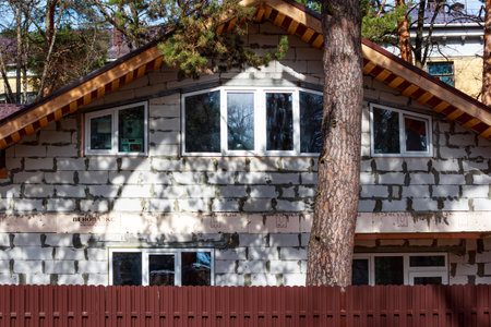 Unfinished house facade built with aerated concrete blocks, featuring white window frames and a prominent pine tree trunk partially obscuring the wall: Russia - March 31, 2024のeditorial素材