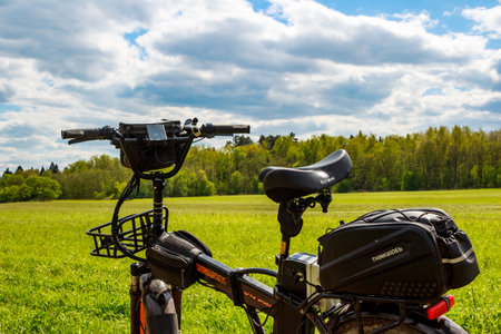 Close-up of a rugged electric bike parked in a vibrant green spring meadow under a bright, cloudy sky: Russia - May 7, 2025のeditorial素材