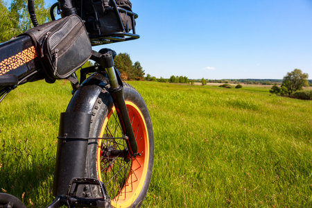 Close-up shot of a fat tire electric bike wheel parked in a vibrant green meadow under a bright blue summer sky: May 22, 2025 - Russiaのeditorial素材