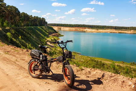 Fat tire electric bike parked on a dusty trail overlooking a brilliant turquoise quarry lake under a sunny blue sky: Russia - May 22, 2025のeditorial素材