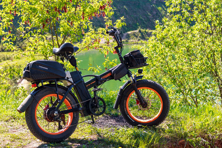 Rugged fat tire electric bike parked outdoors near a vibrant green lake surrounded by lush spring foliage: Russia - May 22, 2025のeditorial素材