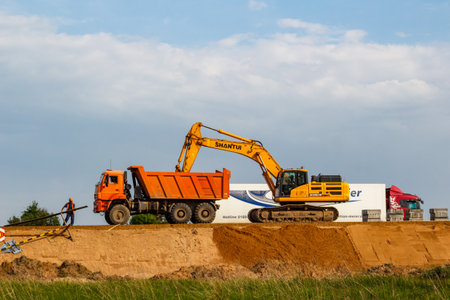 An excavator fills a slope with sand during road works: Kaluga region, Russia - May 29, 2025
