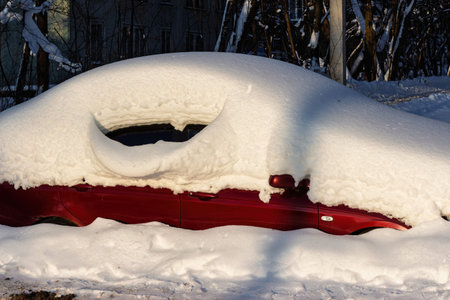Vibrant red auto buried under a vast, pristine mound of powder snow on a crisp, sunny winter day. Epic snowfall challengeの写真素材