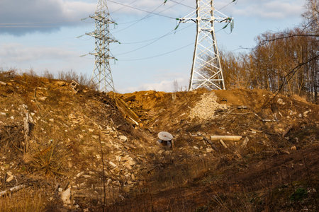 Power lines with tall metal towers rise above a landscape scarred by deforestation and construction debrisの写真素材