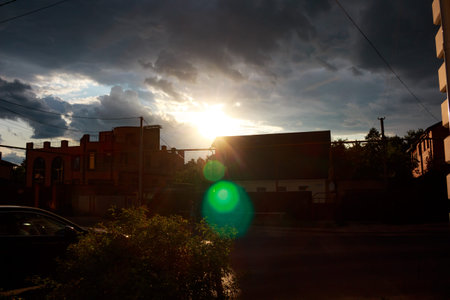 Dramatic sunset or sunrise over a town with dark, cloudy skies and a bright sunburst
