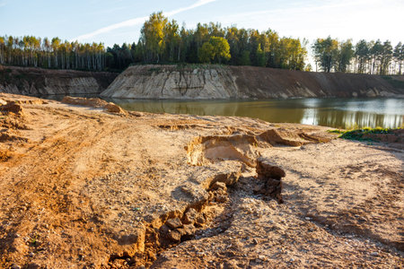 Sunny autumn day landscape with a sandy quarry, green trees on the horizon, and a calm water body...