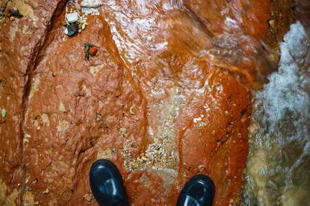 Walking in rubber boots on red clay at the bottom of a streamの写真素材