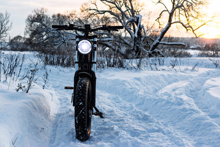 Electric fat bike with glowing headlight cutting through fresh powder at sunset. Winter adventure awaits on this rugged e-bike, perfect for snowy trailsの写真素材