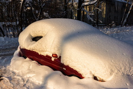 A vibrant red car buried under a massive blanket of pristine white snow on a sunny winter day, showcasing the quiet aftermath of a heavy blizzardの写真素材