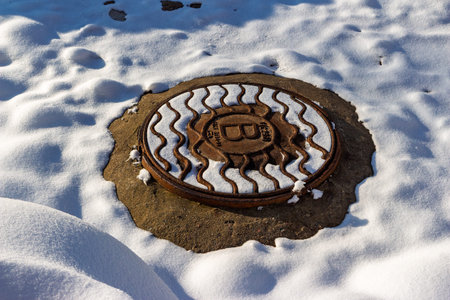 Rusty old cast iron manhole cover partially buried in bright white snow during winter sunshineの写真素材