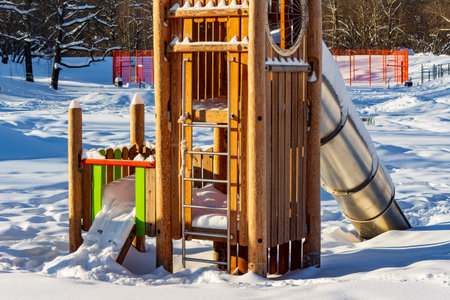 Vibrant wooden playground structure, blanketed in fresh snow, stands brightly under winter sun....