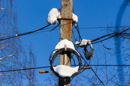 Heavy snow blankets a power pole adorned with intricate wires and communication cables against a...