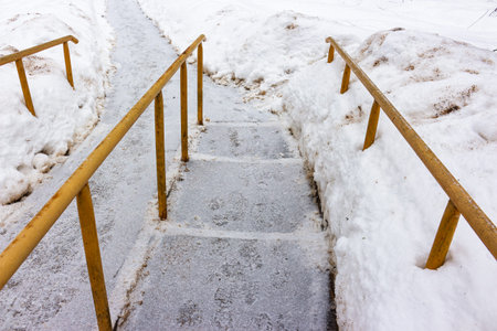 Icy steps descend between snowdrifts, guarded by yellow handrails. A cold winter path, evoking a chilly atmosphereの写真素材