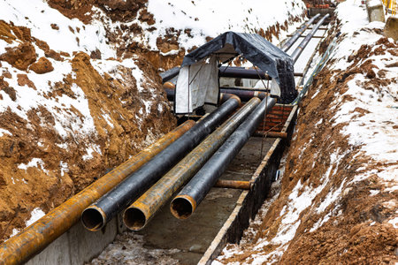 Heavy-duty pipes laid in a snowy trench during utility infrastructure development for new housing...