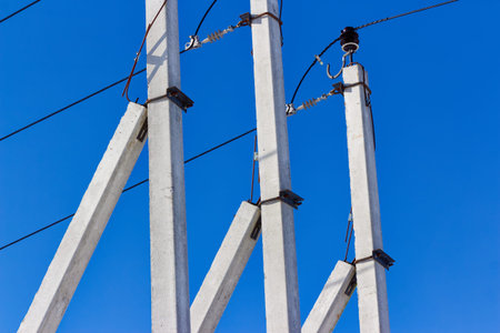 Concrete utility poles carrying three-phase power lines against a clear blue sky, showing electrical infrastructure, high-voltage distribution, and energy transmission hardware