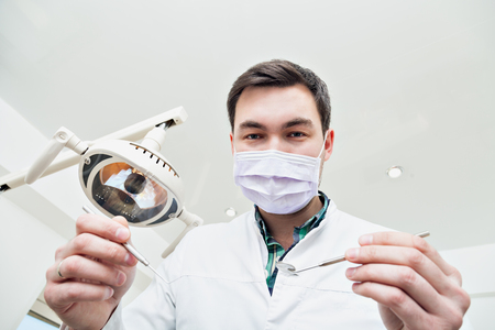 Dentist leaned over the patient. in the dentist's chair in the clinic. The doctor in a mask and with the tool. Admission to the dentist's office.vの写真素材