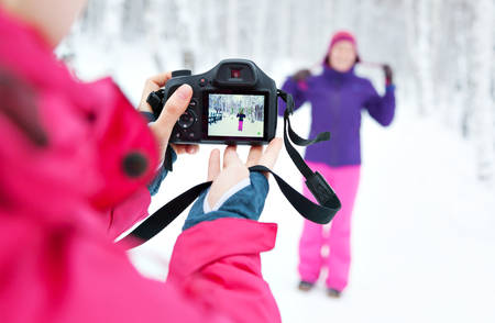 Two girls with a camera taking pictures in snow in winter in a park. Bright jacket. Photographer...