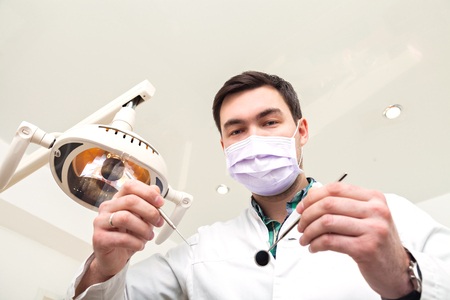 Dentist examining a patients teeth in the dentists chair at the dental clinic. The doctor in a mask and with the tool. Admission to the dentist's office.の写真素材