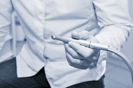 A dentist in a dental clinic. A tool in the hands of the dentist.. Toned image.