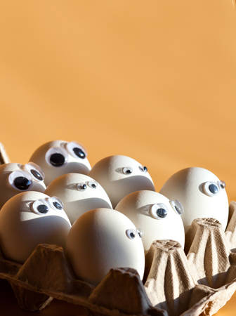 Group of eggs with false eyes looking at you. Eggs in Cortona container on the table. Blye eggs. Breakfast with humor. Preparing for Easter..の写真素材