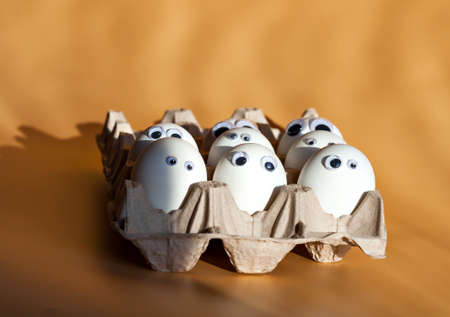 Group of eggs with false eyes looking at you. Eggs in Cortona container on the table. Blye eggs. Breakfast with humor.  Easterの写真素材