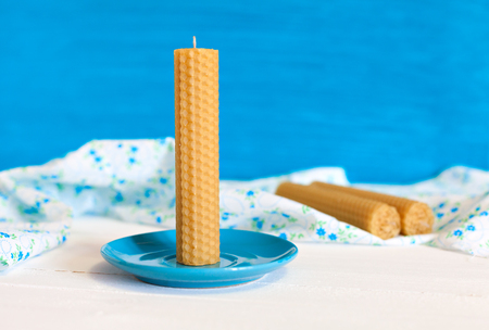 Candle twisted from natural wax by hand on a blue plate. Against the background of the fabric and the other candles. Rustic Style. Gifts with their own handsの写真素材