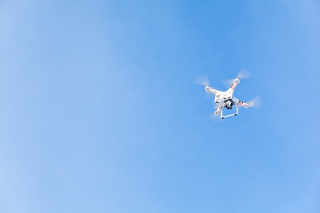 White drone, quadrocopter, with photo camera flying in the blue sky. Concept