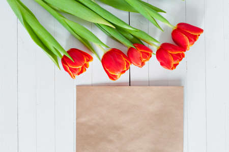 Red tulips with blank greeting card on a white wooden table. Envelope kraft paper. View from above.の写真素材