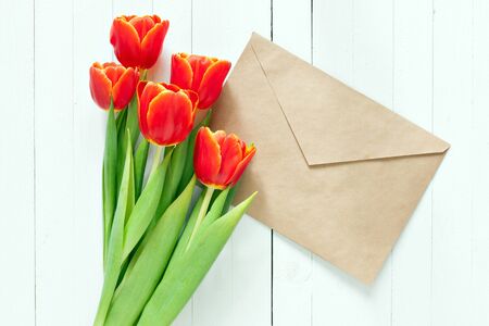 Red tulips with blank greeting card on a white wooden table. Envelope kraft paper. View from above.の写真素材