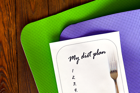 Diet plan on a white sheet of paper. The new list and yoga mat green and purple on a wooden background. Weight loss and fitness. for dinner fork. The concept of love to a healthy lifestyle.の写真素材
